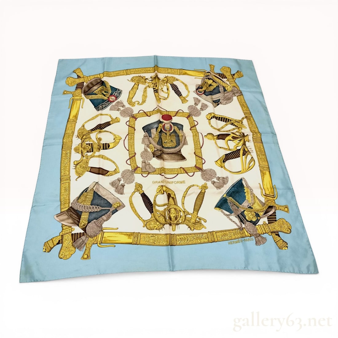 Hermes Grand Uniforme Silk Scarf by Joachim Metz: Hermes silk scarf in the Grand Uniforme pattern designed by Joachim Metz, first issued in 1985. The motif depicts historical military ceremonial sabers and shakos on a cream field with a light blue bo