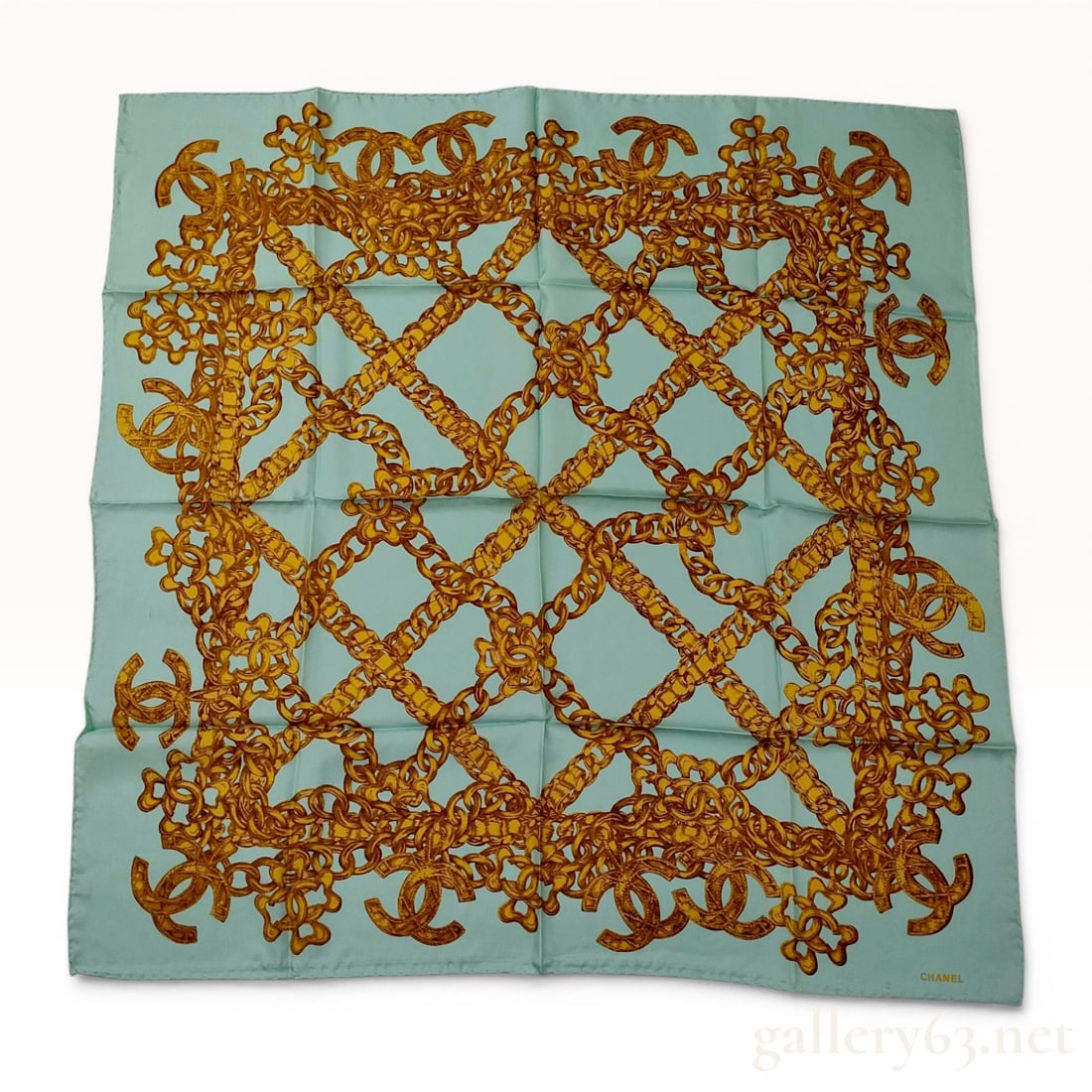 Chanel Vintage Chain-Link Print Silk Scarf: Vintage Chanel square silk scarf featuring a gold-toned chain-link lattice pattern with interlocking CC logos on an aqua ground. The 100% silk piece is finished with hand-rolled edges and includes a p