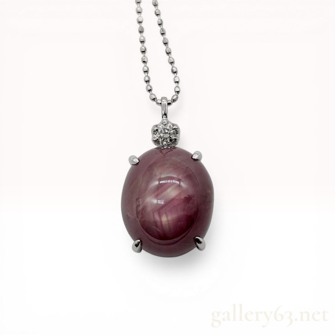 Platinum & 18K White Gold Star Ruby and Diamond Pendant Necklace: Platinum pendant featuring a large oval cabochon star ruby and a round brilliant-cut diamond accent. The ruby is held in a four-prong setting and exhibits a six-rayed asterism, while the diamond is se