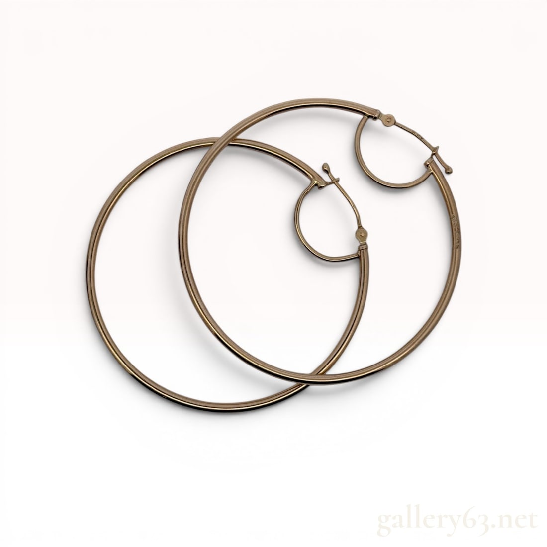 A Pair of Italian 10K Yellow Gold Large Tubular Hoop Earrings: A matched pair of large round hoop earrings of Italian manufacture. Each earring features a hollow tubular construction in 10-karat yellow gold with a hinged saddle-back closure and snap-down wire. Th