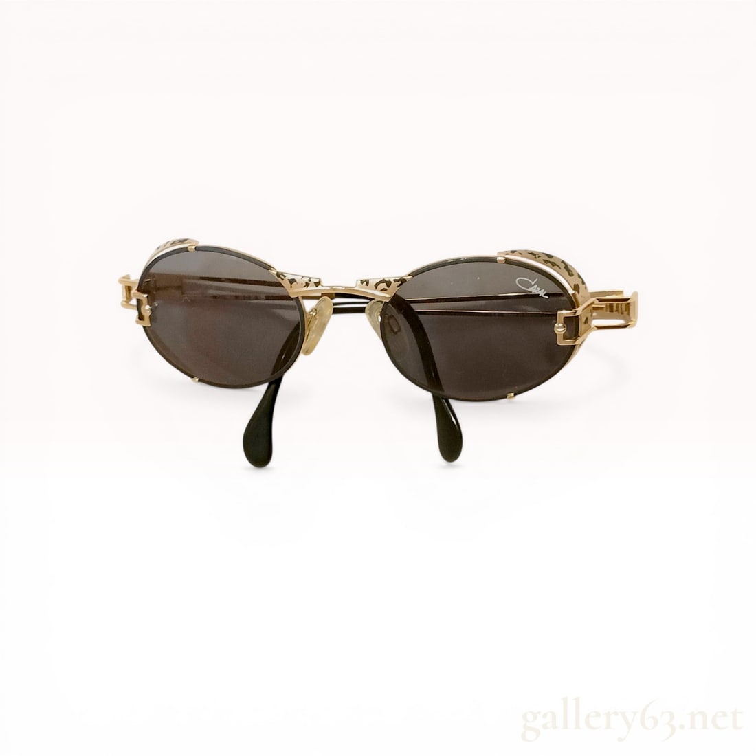Cazal Vintage Gold Toned Oval Sunglasses with Leopard Pattern: Vintage Cazal sunglasses, late 20th century. Features an ornate gold-toned metal frame with oval tinted lenses, leopard-patterned rim accents, and architectural split-bar temples with black acetate ti