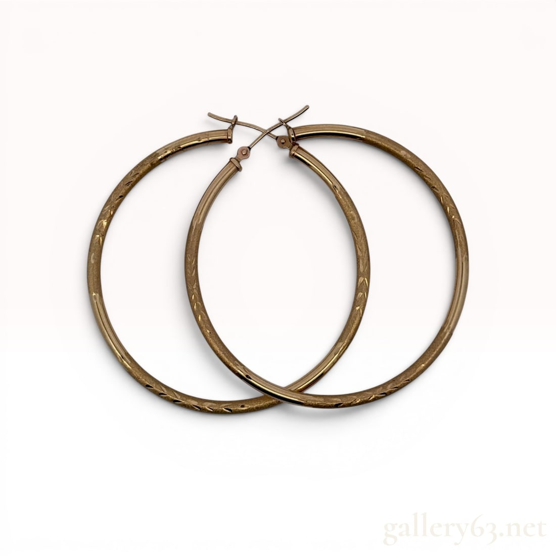 A Pair of 10 Karat Yellow Gold Patterned Hoop Earrings: A pair of 10 karat yellow gold large hoop earrings featuring a hinged latch-back closure. Each hoop exhibits a brushed matte finish accented with a diamond-cut foliate motif. The hinged posts are stam