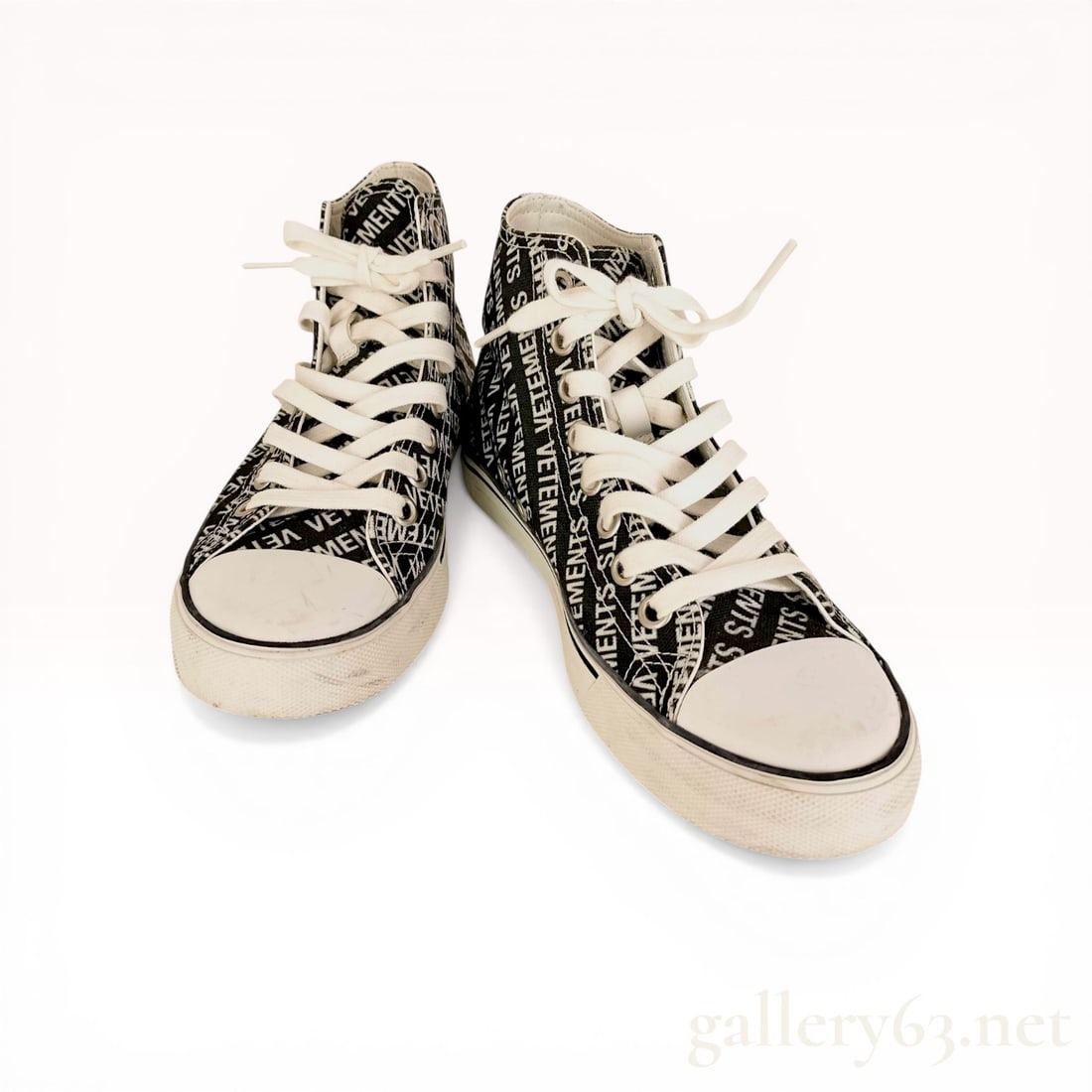 A Pair of Vetements Printed Canvas High-Top Sneakers: Vetements printed canvas high-top sneakers, contemporary. Features a black canvas upper with an all-over white diagonal logo print, white rubber toe caps, and white midsoles with black racing stripes 