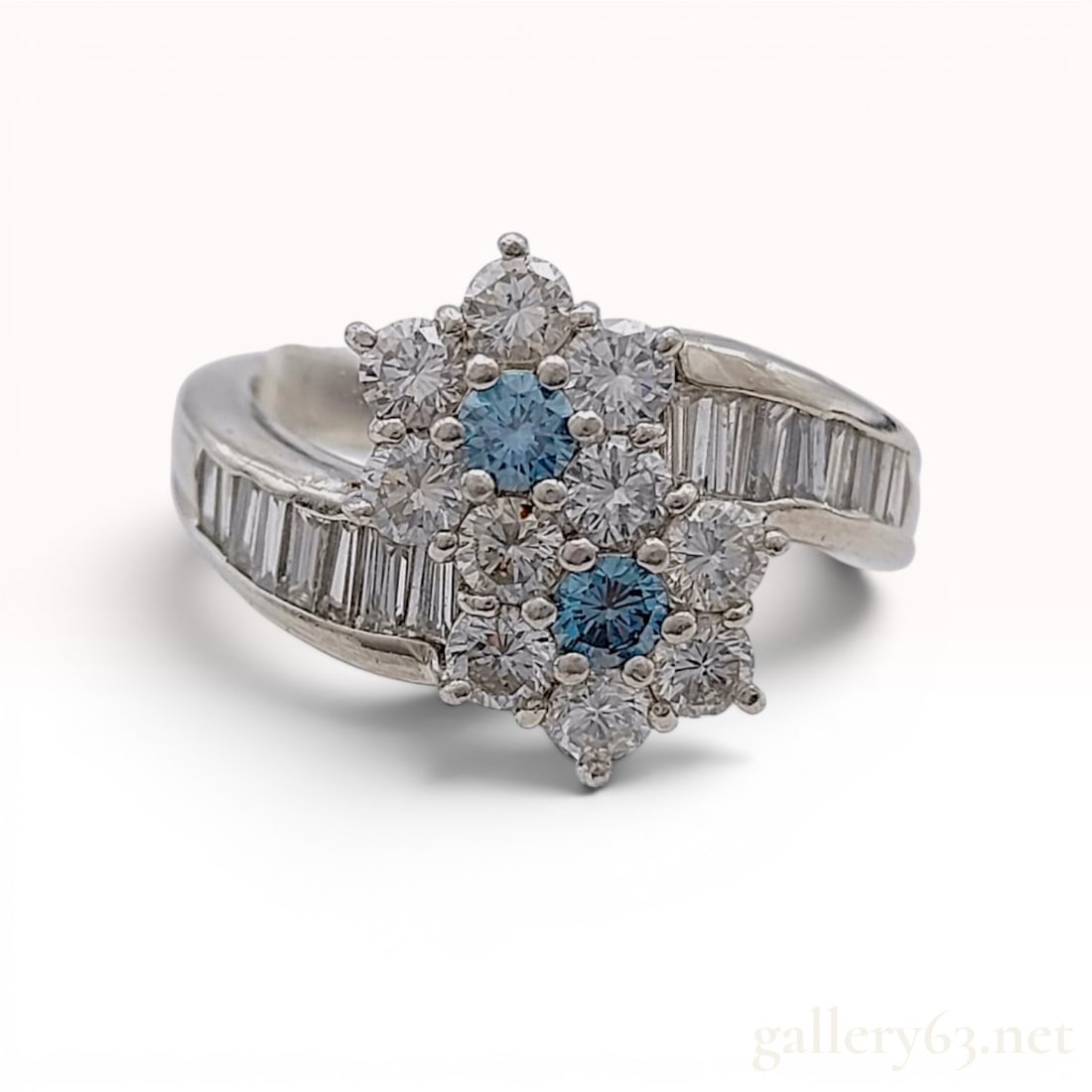 Platinum Blue and Clear Stone Bypass Cluster Cocktail Ring: Platinum bypass cocktail ring featuring two floral clusters centered with round brilliant-cut blue stones and bordered by round brilliant-cut clear stones. The bypass shoulders are channel-set with ap