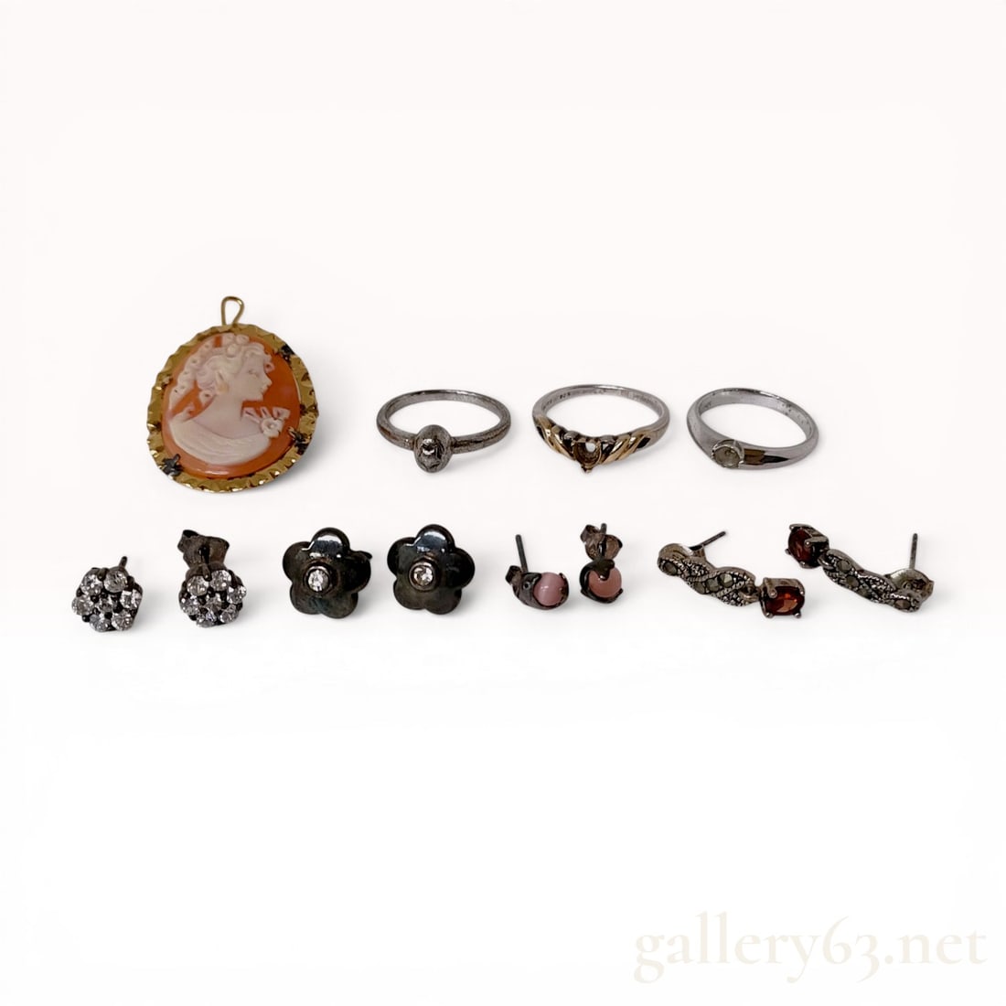 An Assortment of Jewelry Including a Shell Cameo Brooch and Sterling Silver Rings: This collection features a variety of jewelry pieces, headlined by a carved shell cameo depicting a woman in left-facing profile with floral details. The cameo is set in a gold-tone metal frame with a