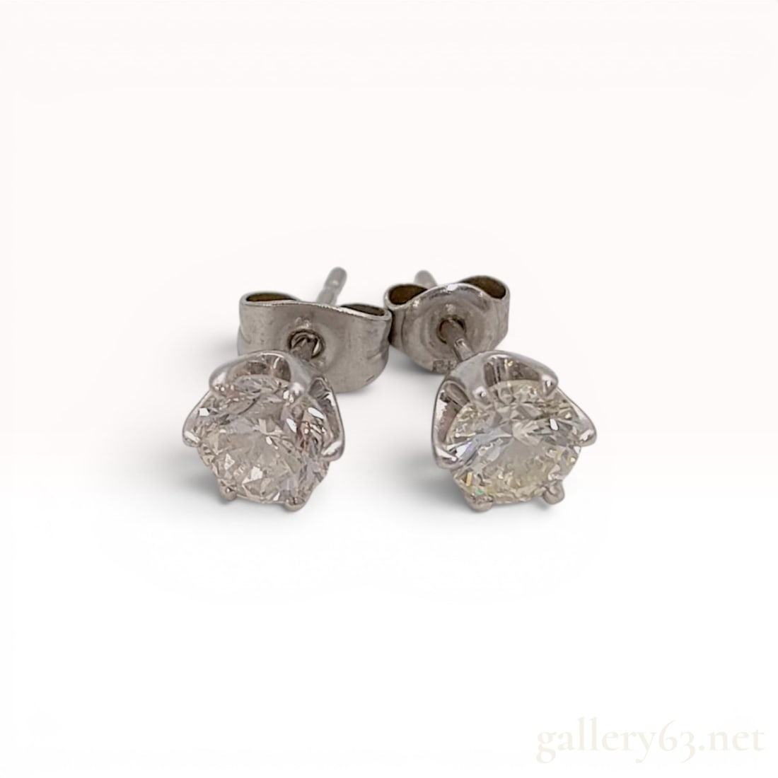 A Pair of 1.5ctw Platinum and Round Brilliant Cut Colorless Natural Diamond Stud Earrings: A matched pair of diamond stud earrings featuring two round brilliant-cut natural diamonds. Each stone is secured in a six-prong platinum basket setting. The settings are hallmarks with Pt900, and the
