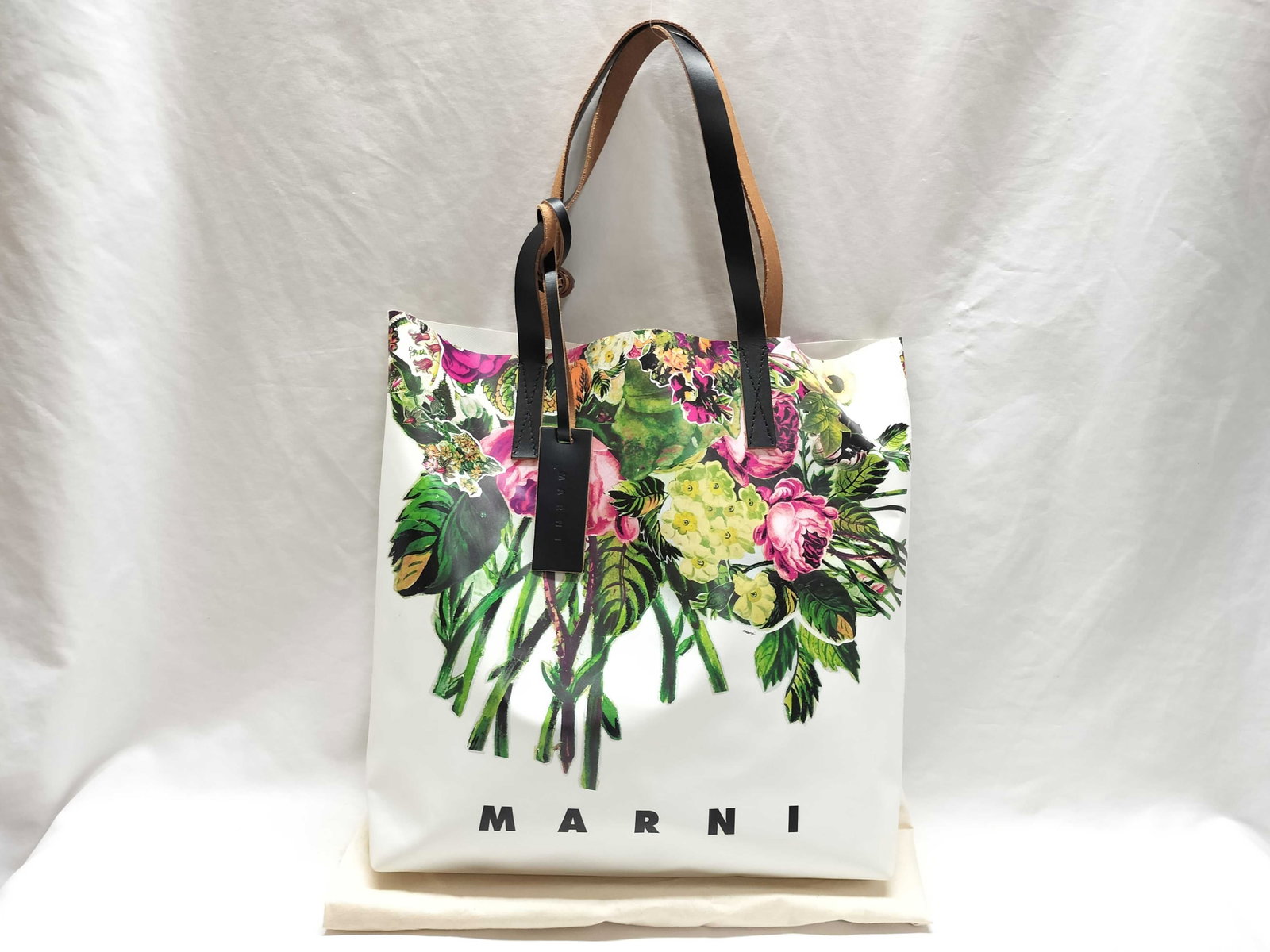 Marni Tribeca Floral Print PVC Shopper Tote Bag: This Marni Tribeca N/S shopper tote bag is constructed from a white coated PVC fabric featuring a vibrant multicolor floral bouquet print on the front. The bag has an open-top design and an unlined in