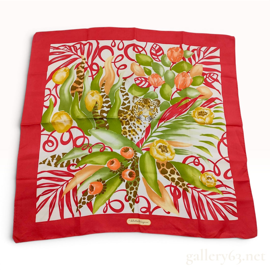 Salvatore Ferragamo Leopard and Jungle Motif Silk Scarf: A square silk scarf designed by Salvatore Ferragamo featuring a vibrant jungle-themed illustration. The central composition depicts a leopard peering through dense tropical foliage consisting of large