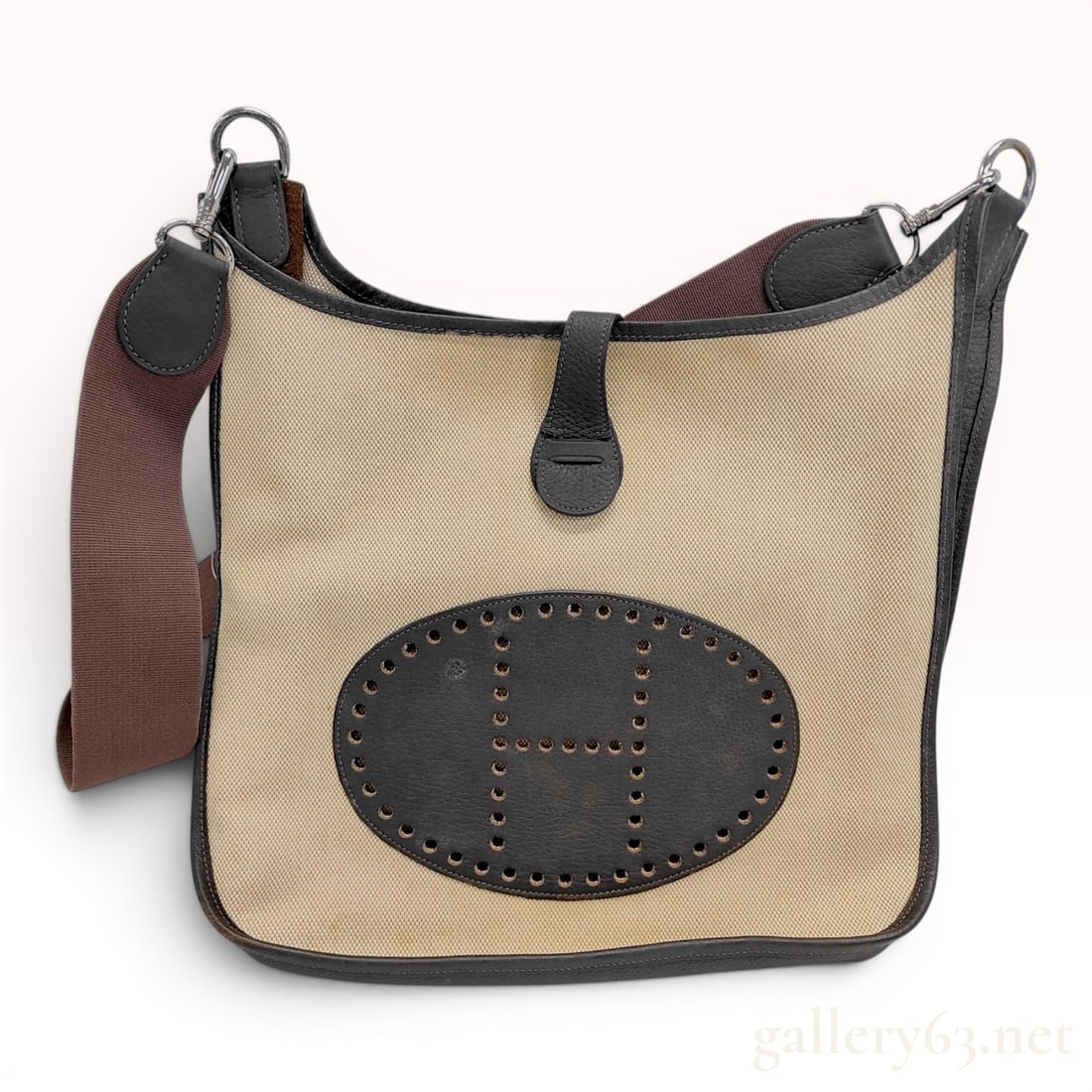 Hermes Evelyne PM Toile and Grained Leather Crossbody Bag: An Hermes Evelyne PM crossbody handbag featuring a beige toile canvas body accented by dark brown grained leather trim. The front of the bag displays the signature perforated H logo set within a stitc