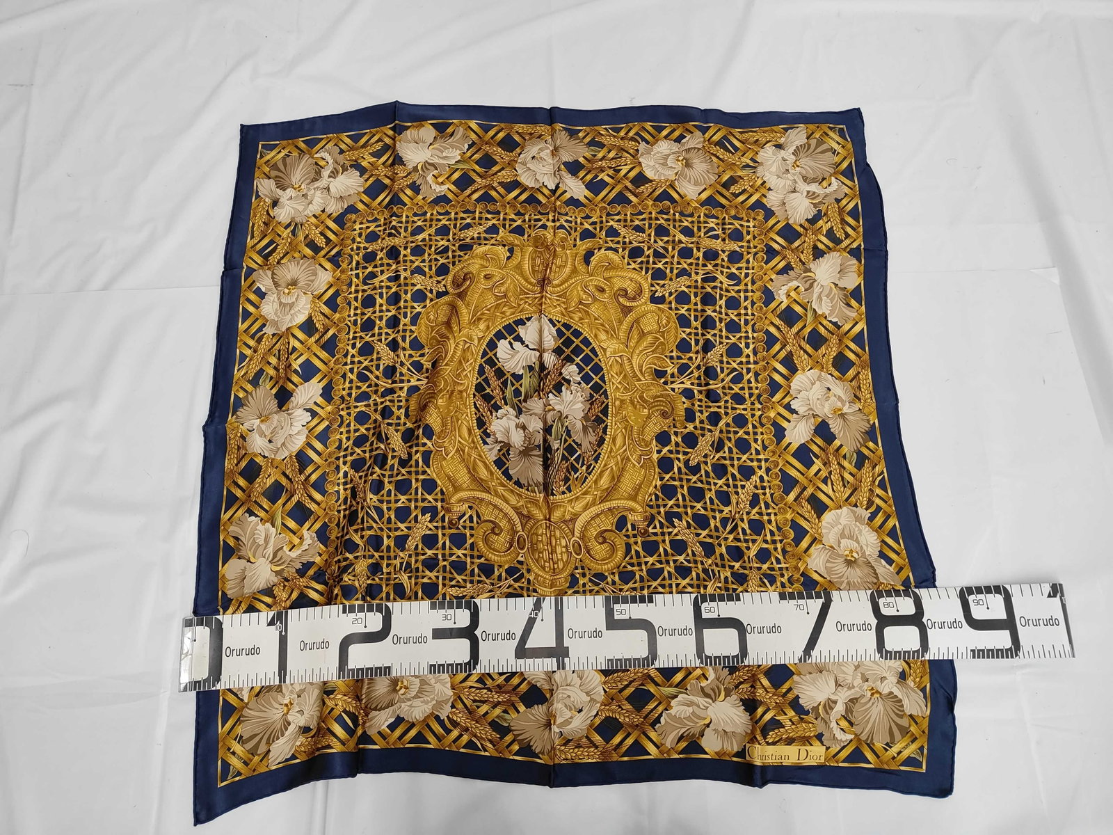 Christian Dior Vintage Navy and Gold Silk Scarf with Iris and Wheat Motif: A square silk scarf by Christian Dior featuring a botanical and floral design in navy blue, gold, and white. The central composition consists of an oval medallion depicting a bouquet of white irises a
