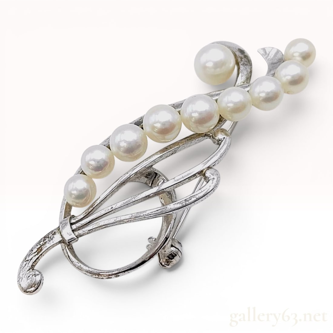Mikimoto Sterling Silver and Graduated Cultured Pearl Spray Brooch: A vintage spray brooch by Mikimoto, crafted in sterling silver. The piece features a stylized curved branch or floral spray design set with eleven graduated white cultured pearls. The pearls display h
