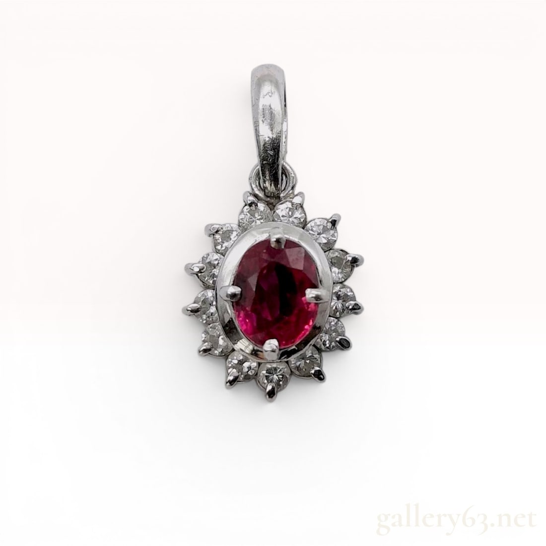 Platinum .47ct Ruby and .182ctw Diamond Halo Pendant: This platinum halo style pendant features a centrally set oval faceted pinkish-red ruby in a four-prong setting. The ruby is surrounded by a cluster of round brilliant-cut diamonds and the mounting is