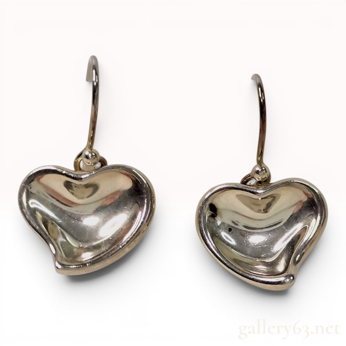 A Pair of Tiffany and Co. Elsa Peretti Sterling Silver Full Heart Drop Earrings: This matched pair of drop earrings is designed by Elsa Peretti for Tiffany and Co. in the Full Heart motif. Each earring features an organic, asymmetrical puffed heart charm suspended from a curved fi