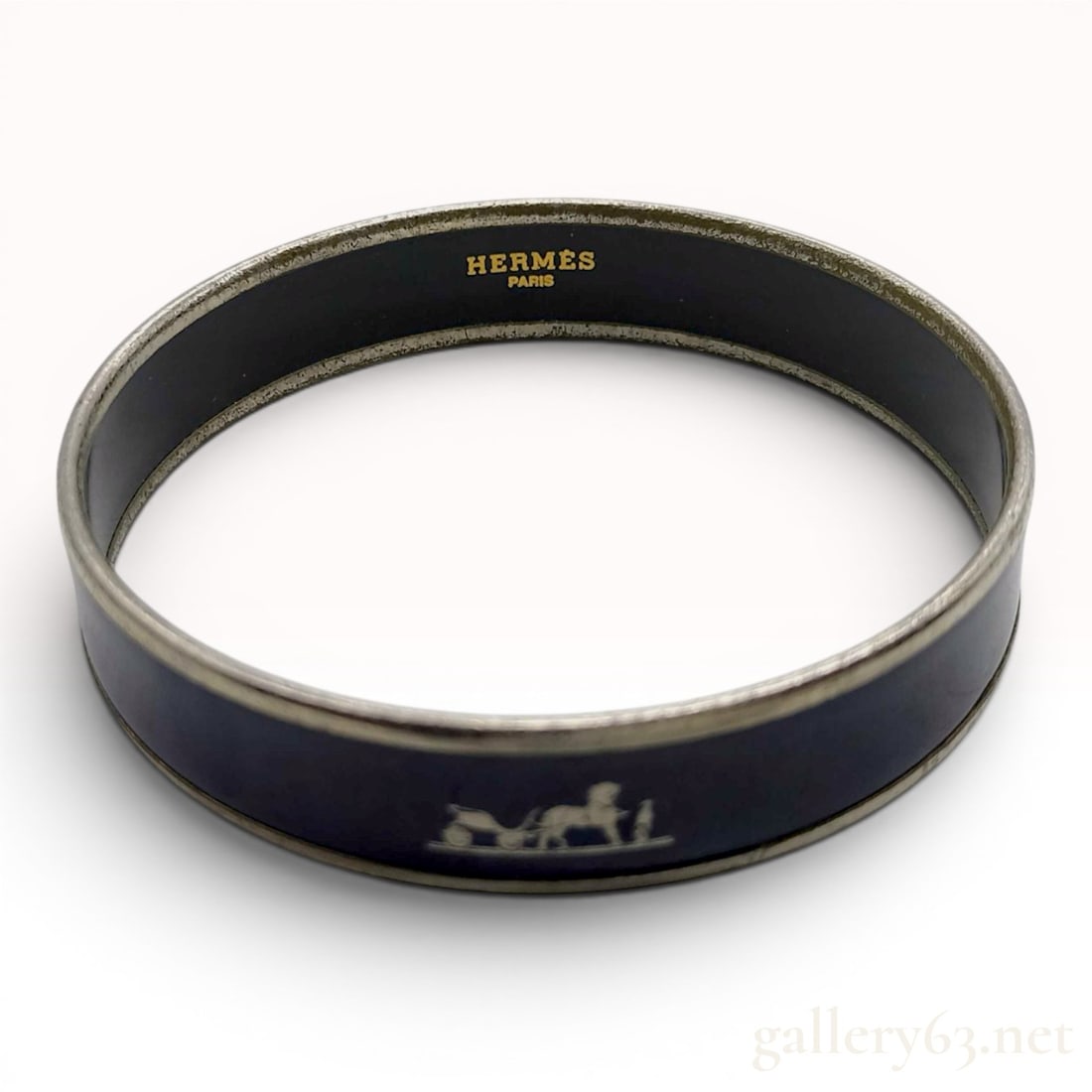 Hermes Narrow Navy Enamel Caleche Bangle Bracelet: This Hermes Caleche narrow bangle features a navy blue enamel band set within silver-tone metal rims. The exterior surface is detailed with the brand signature horse and carriage motif in a silver-col