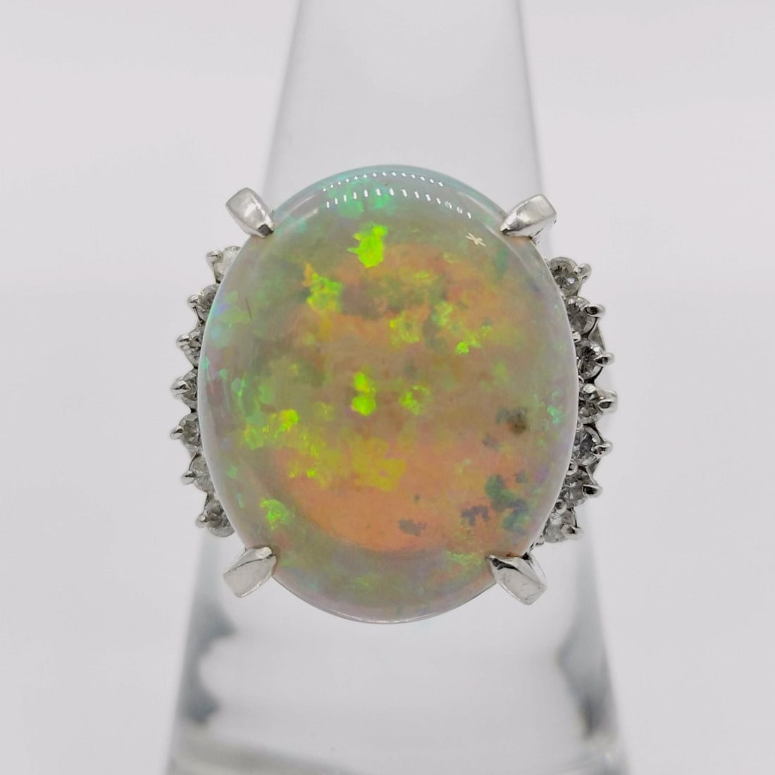 Platinum Oval Opal and Diamond Cocktail Ring: This platinum cocktail ring features a large centrally mounted oval cabochon-cut natural opal. The stone exhibits a vibrant play-of-color with flashes of green, orange, and yellow throughout a translu