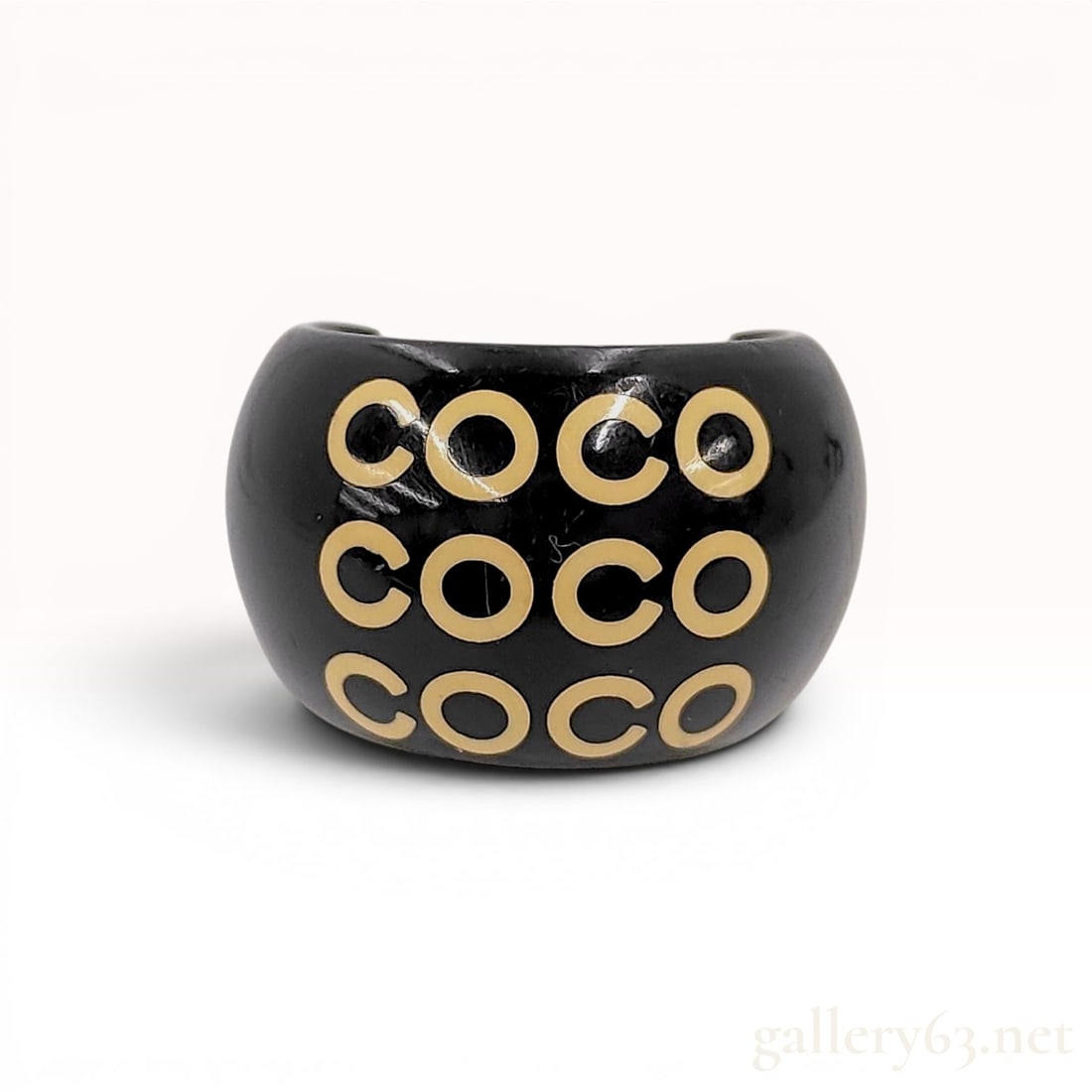 Coco Chanel Black Resin Wide Dome Ring: Chanel wide open-back dome ring crafted from black glossy resi. The design features three horizontal rows of the word COCO in cream-colored inlay across the front face. A white interlocking CC logo is