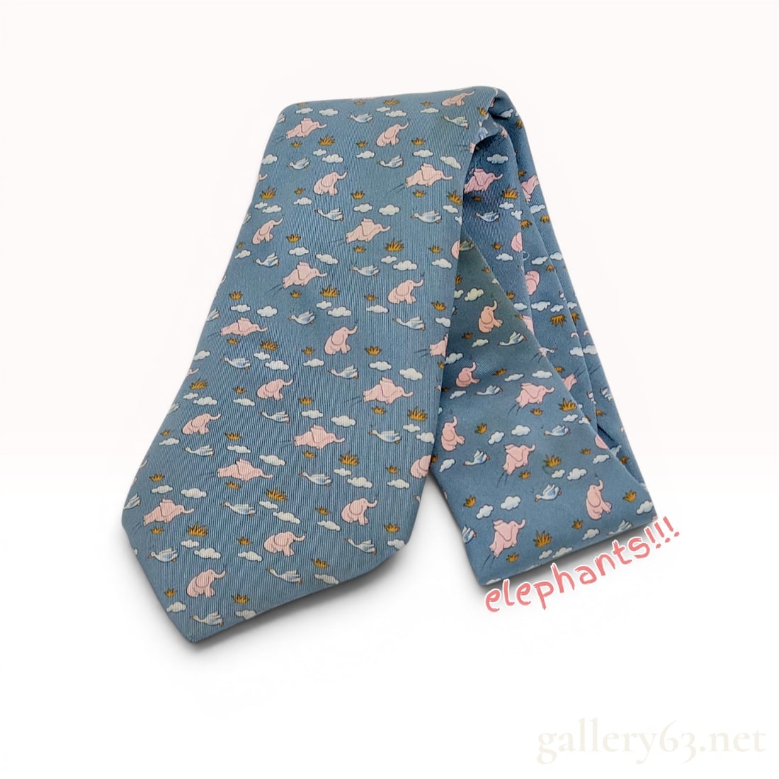 Hermes Blue Silk Flying Elephant Print Necktie: This Hermes necktie is crafted from 100 percent silk in a blue twill weave. The design features a repeating whimsical print of pink flying elephants, white birds, stylized clouds, and small tufts of y