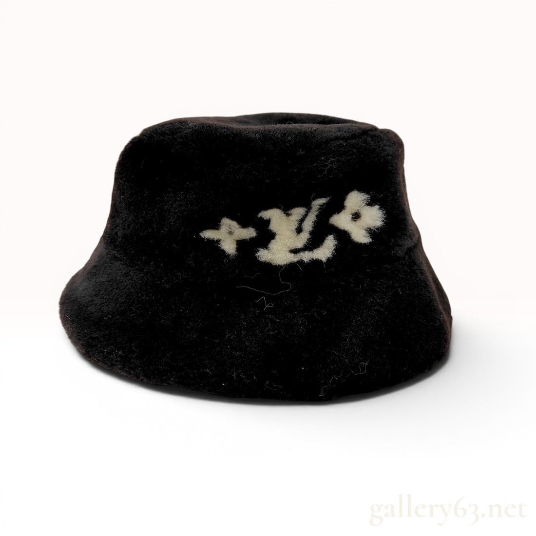 Louis Vuitton Shearling Monogram Bucket Hat: This contemporary Louis Vuitton bucket hat is crafted from a dark, plush shearling sheepskin. The front features an inset cream-colored monogram consisting of the letters L and V flanked by two floral