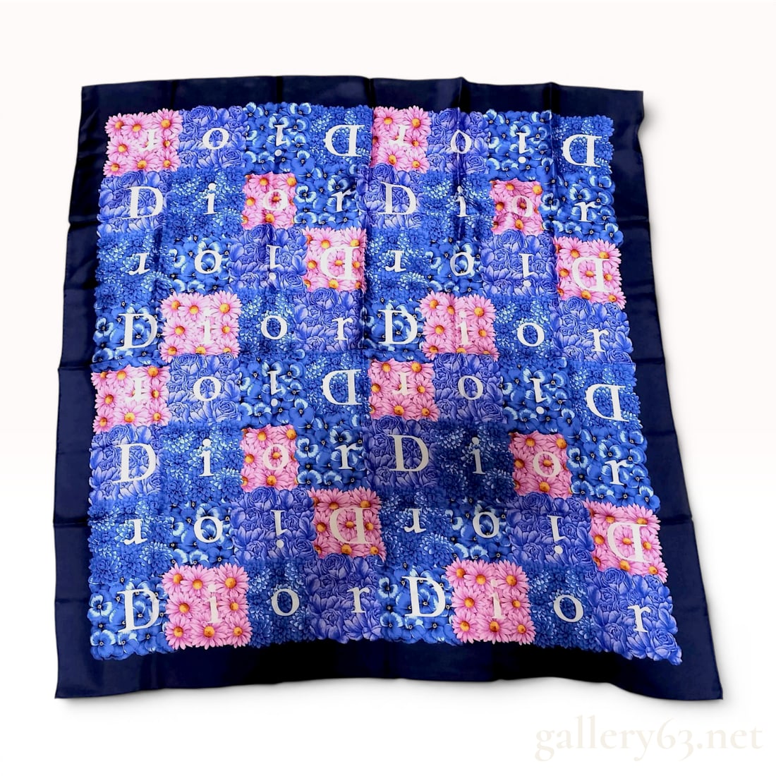 Christian Dior Floral and Logo Monogram Silk Scarf: This square silk scarf from Christian Dior features a dense, vibrant floral mosaic pattern composed of pink and blue blossoms. Interspersed throughout the central floral field is the name Dior in whit