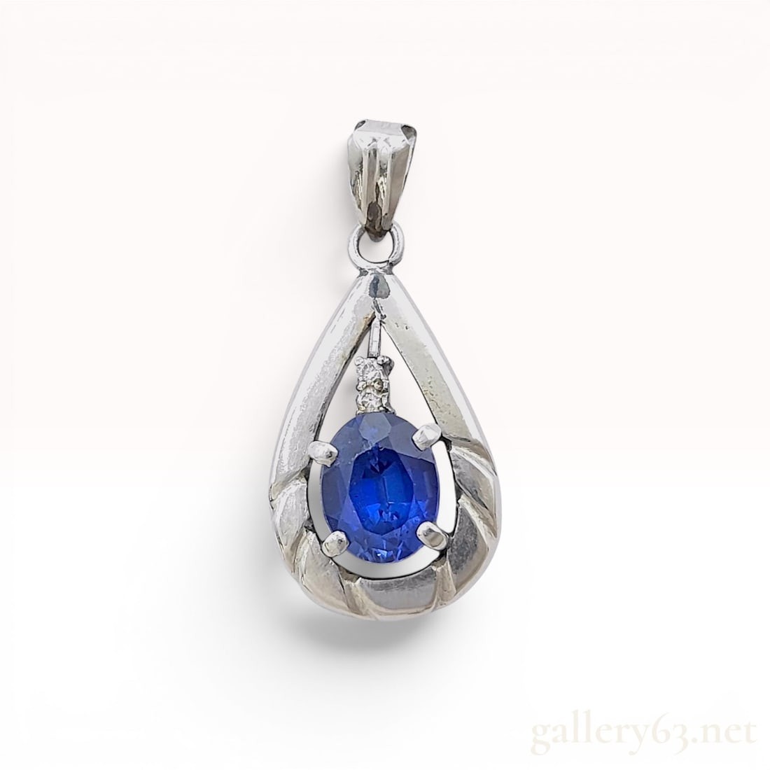 Platinum 900 Blue Sapphire and Diamond Teardrop Pendant, 1.85 Carats: A teardrop-shaped pendant crafted from Platinum 900 featuring a central oval-cut blue sapphire weighing 1.85 carats. The sapphire is held in a four-prong basket setting within an open-frame design. Tw