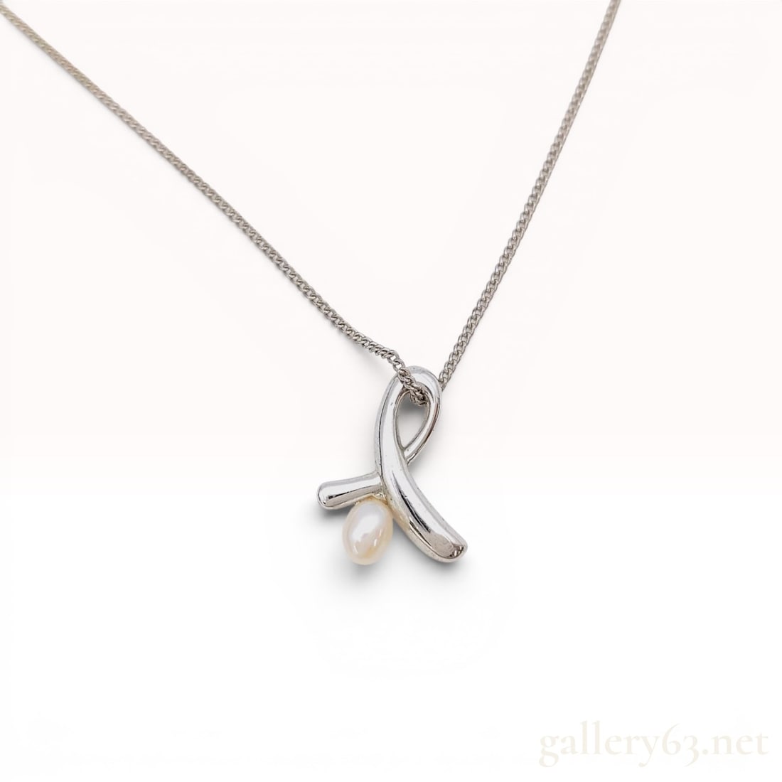 Tasaki Silver and Pearl Ribbon Motif Pendant Necklace: A silver and pearl pendant necklace by Tasaki. The pendant is designed in a stylized ribbon motif with a polished finish and features a single white cultured pearl in an oval or teardrop shape mounted