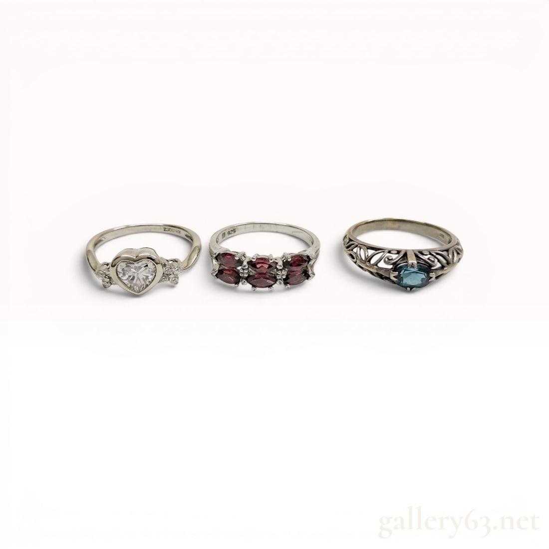 A Trio of Sterling Silver and Gemstone Rings: A collection of three sterling silver rings featuring various settings and synthetic or semi-precious gemstones. The lot includes a Diamonique ring with a heart-shaped cubic zirconia, a band set with 