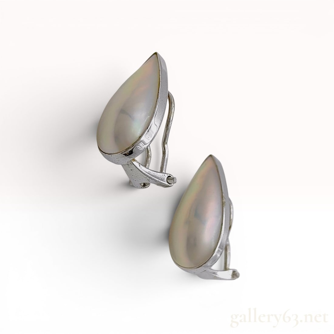 A Pair of Tasaki 14K White Gold and 19.5*9.6mm Pearl Earrings: A matched pair of 14 karat white gold and mother-of-pearl clip-on earrings. Each earring features a bezel-set pear-shaped mother-of-pearl cabochon displaying characteristic iridescence. The settings a