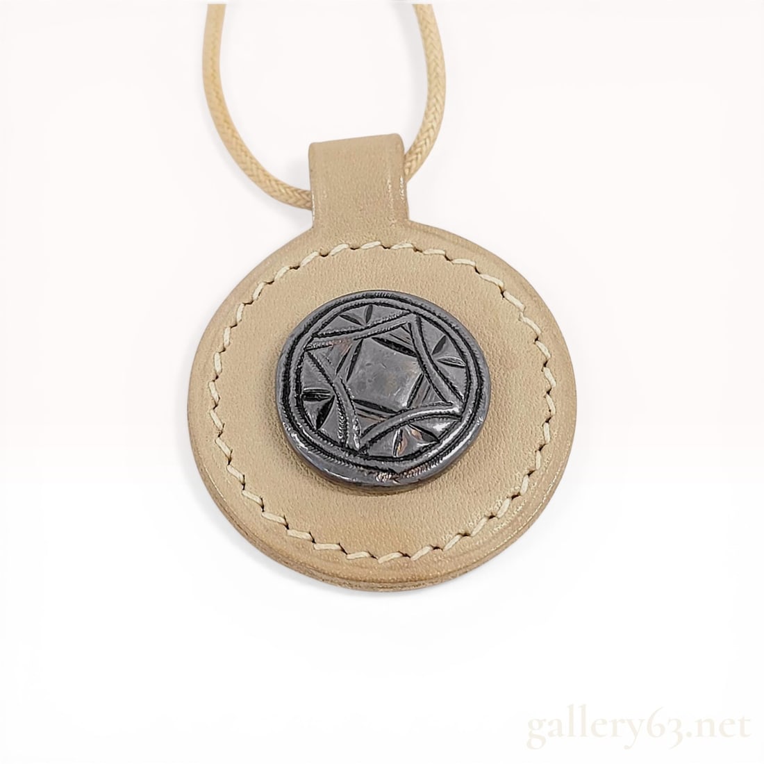 Hermes Leather and Metal Talisman Pendant Necklace, 2009: Hermes circular leather and metal talisman pendant necklace, dated 2009. The tan leather pendant features cream contrast stitching and an inset patinated metal disk with a geometric star motif, suspen