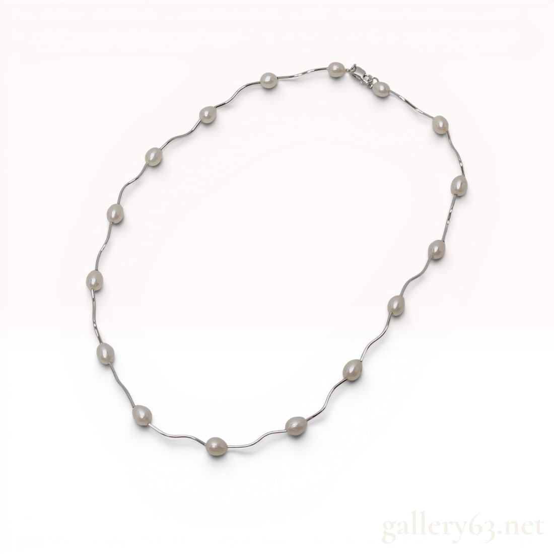 Sterling Silver and Freshwater Pearl Wavy Station Necklace: Modern sterling silver station necklace featuring fourteen oval white freshwater pearls. The pearls are spaced evenly and connected by curved, wavy polished silver bar links. The piece is secured by a