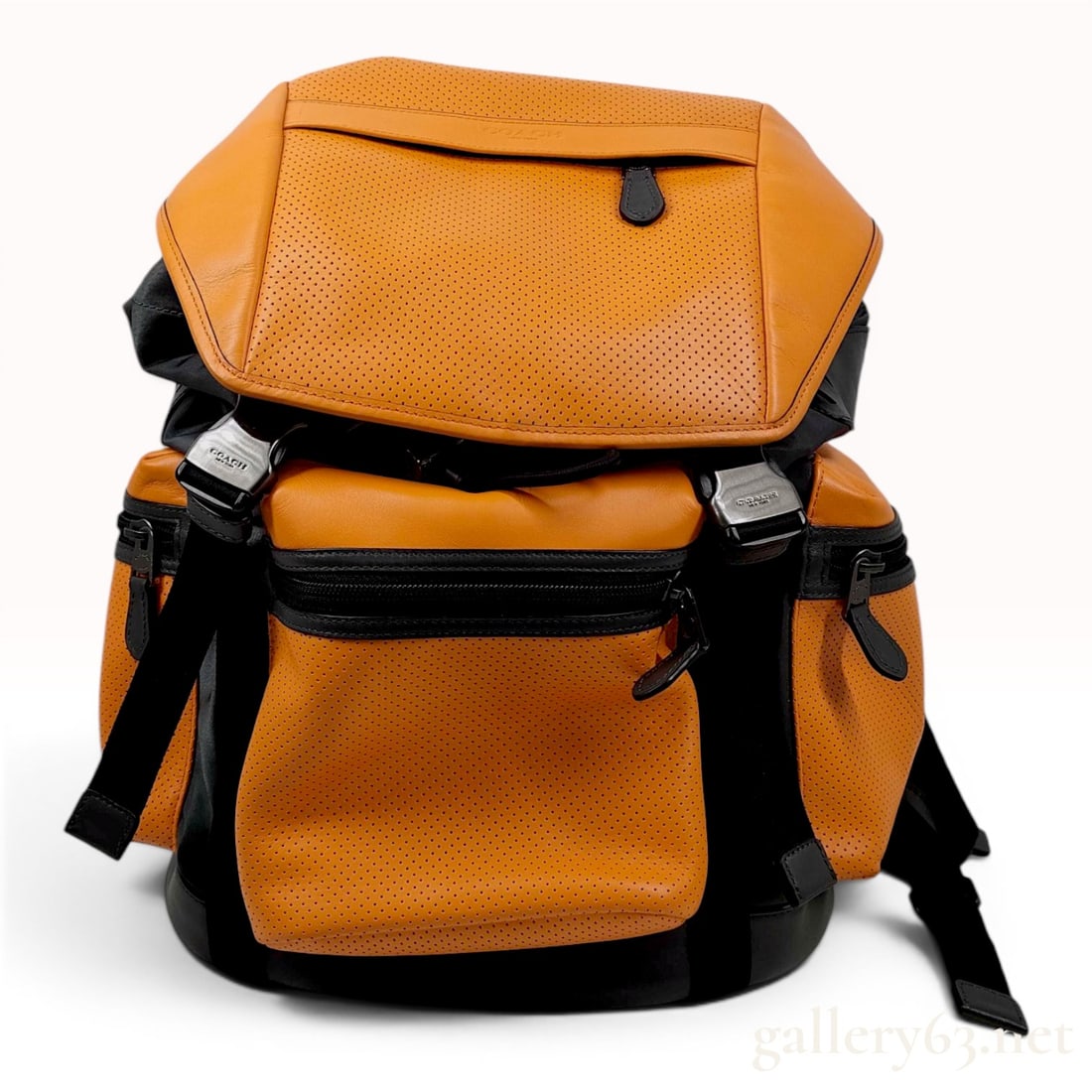 Coach Terrain Trek Pack in Perforated Mixed Materials: A Coach Terrain Trek Pack technical rucksack featuring a vibrant orange perforated leather body contrasted with smooth charcoal grey leather and black nylon accents. The design includes a large top fl