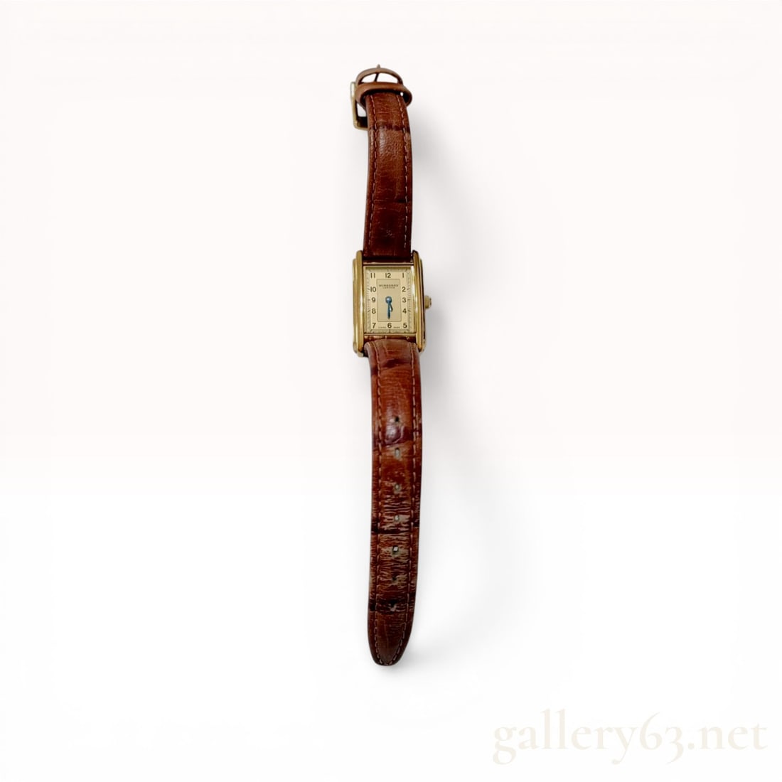 Burberry London Ladies Quartz Tank Watch Model 12100L: Burberry London ladies' tank-style wristwatch, model 12100L. The timepiece features a gold-tone rectangular case housing a cream dial with black Arabic numerals and blued steel baton hands. It is equi