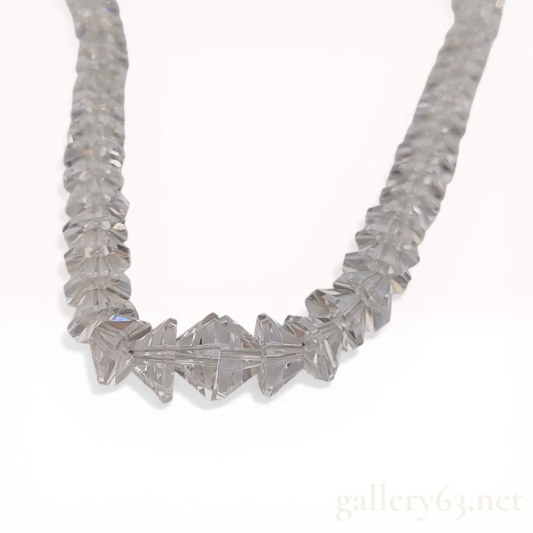 Graduated Faceted Quartz Beaded Necklace with Silver Clasp: A beaded necklace composed of graduated faceted bicone-shaped colorless quartz beads. The strand is secured by a silver box clasp featuring a cast floral motif. The reverse of the clasp is embossed wi