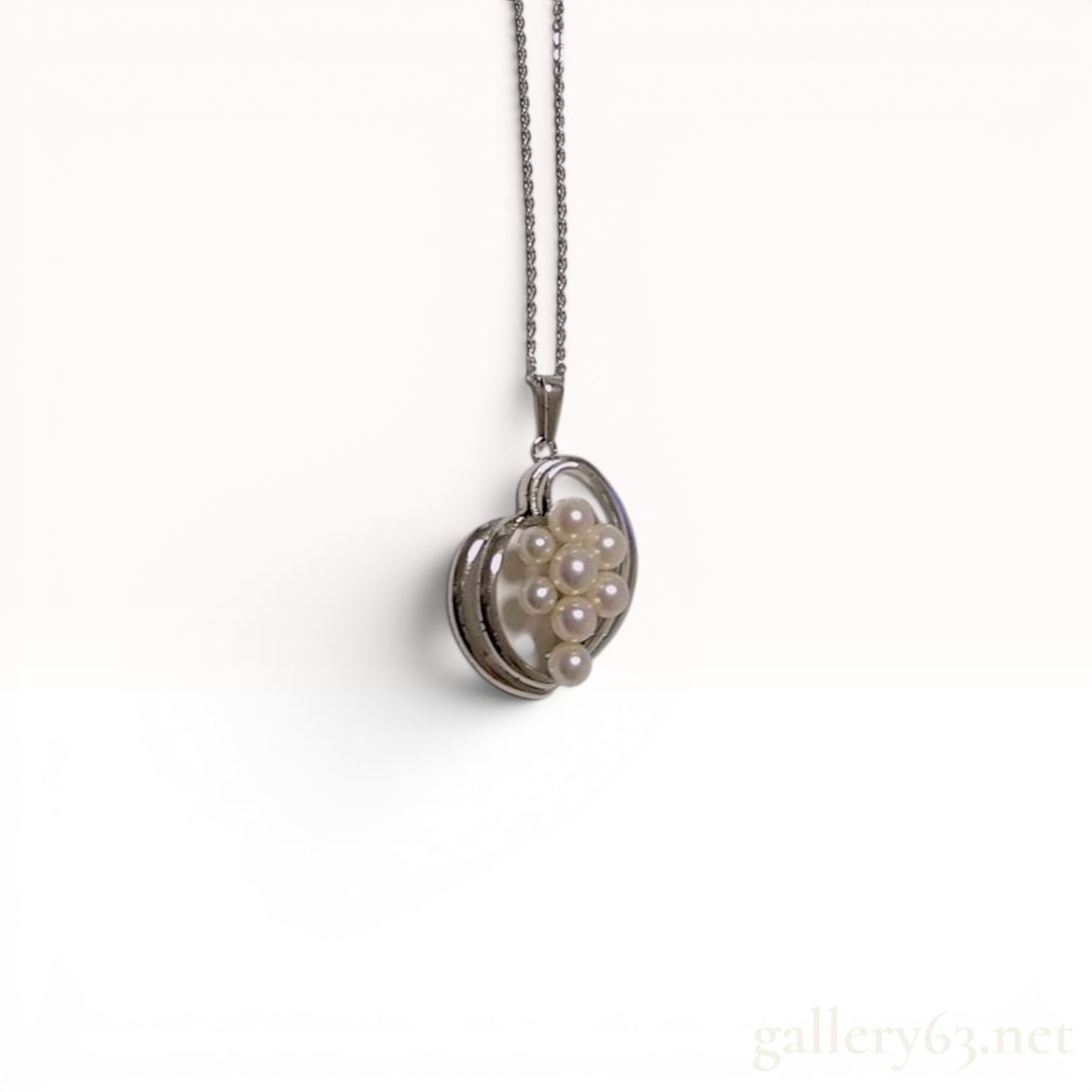 A Trio of Silver Jewelry Items Including a Mikimoto Cultured Pearl Necklace: A trio of silver jewelry items featuring a Mikimoto cultured pearl pendant necklace, a gemstone tie tack, and an abstract rectangular pendant. The Mikimoto necklace features a silver heart-shaped swir