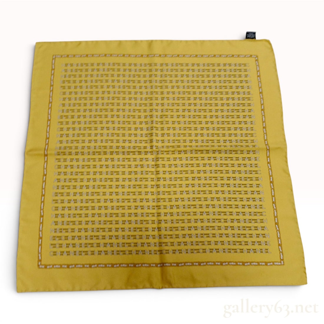 Chanel Repeating Logo and Chain Motif Silk Pocket Square: This Chanel silk pocket square features a bright yellow ground with a central field of repeating horizontal "CHANEL" wordmarks in a white or silver-tone print. The pattern is framed by a printed borde