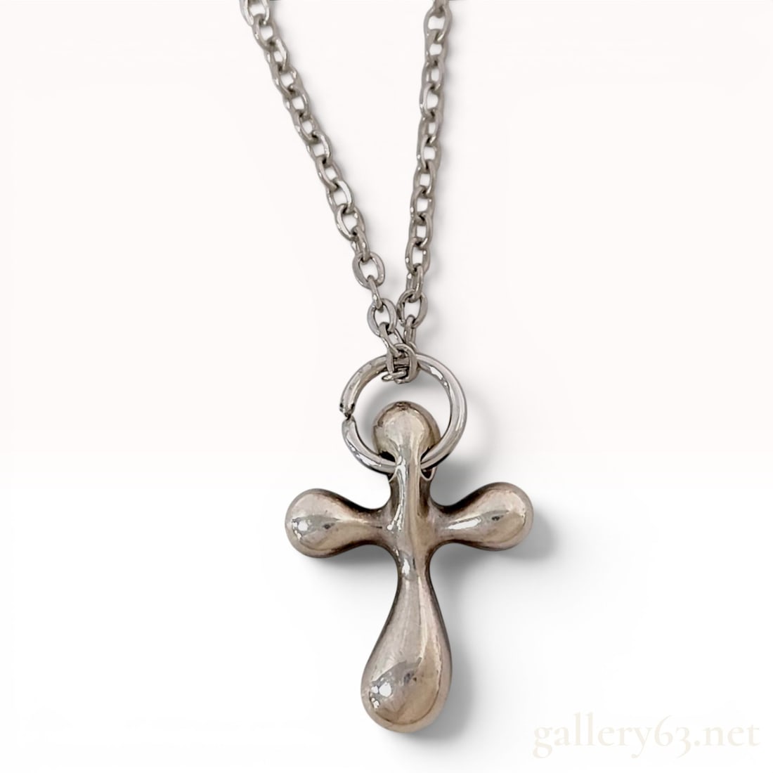 Stainless Steel Small Cross Pendant Necklace in the Style of Elsa Peretti: A necklace featuring a stainless steel pendant designed in the organic, fluid form of the Elsa Peretti small cross for Tiffany and Co. The pendant consists of four rounded, bulbous arms in a stylized 