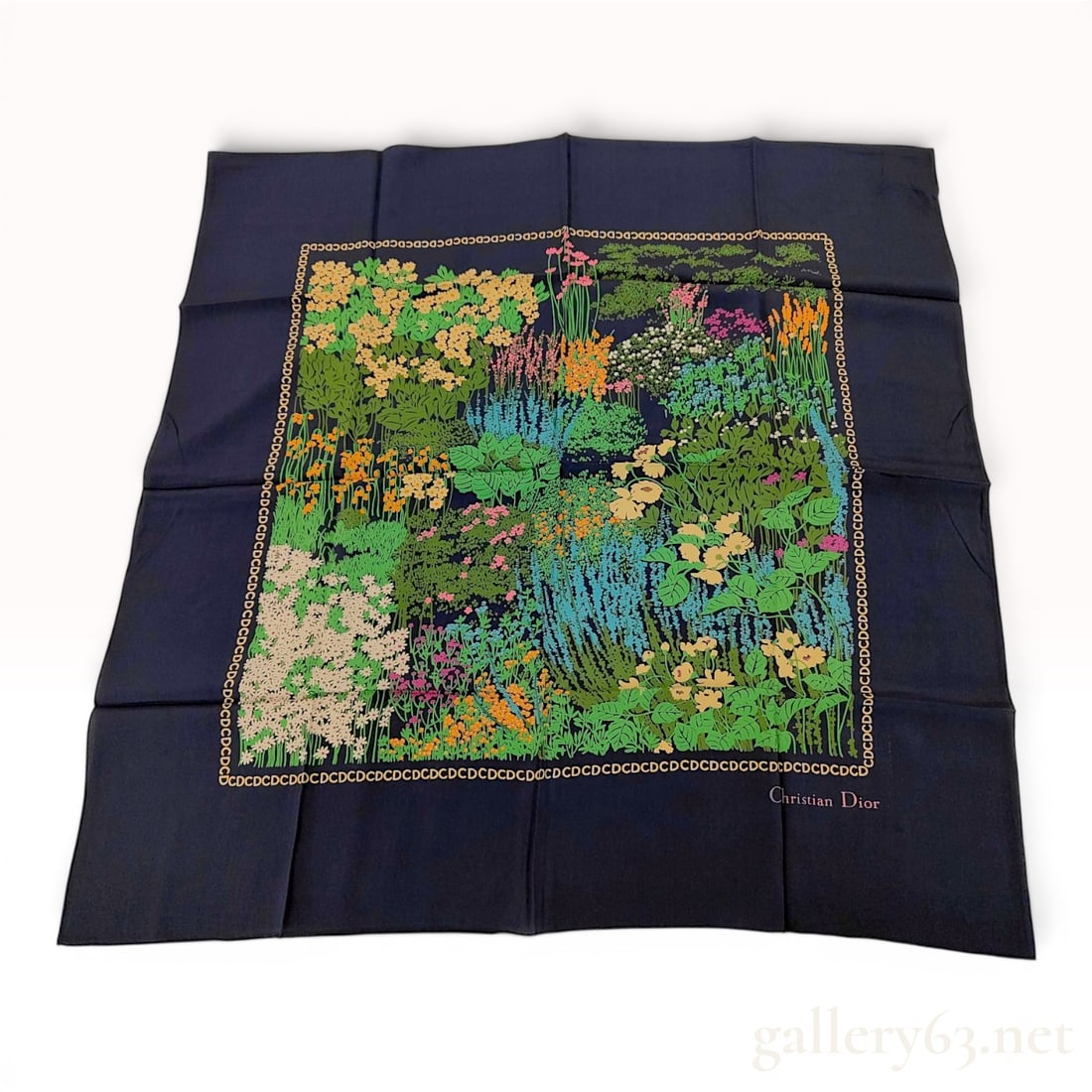 Christian Dior Floral Garden Silk Scarf with Monogram Border: This square silk scarf by Christian Dior features a central botanical illustration of a garden scene. The multi-colored pattern depicts a variety of flowers and foliage in shades of green, yellow, ora