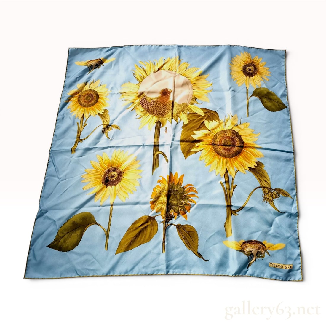 Tiffany and Co. Sunflower Print Silk Square Scarf: A 100 percent silk square scarf by Tiffany and Co. featuring a botanical sunflower motif. The design presents various sunflowers in multiple stages of bloom and orientations against a light sky-blue b