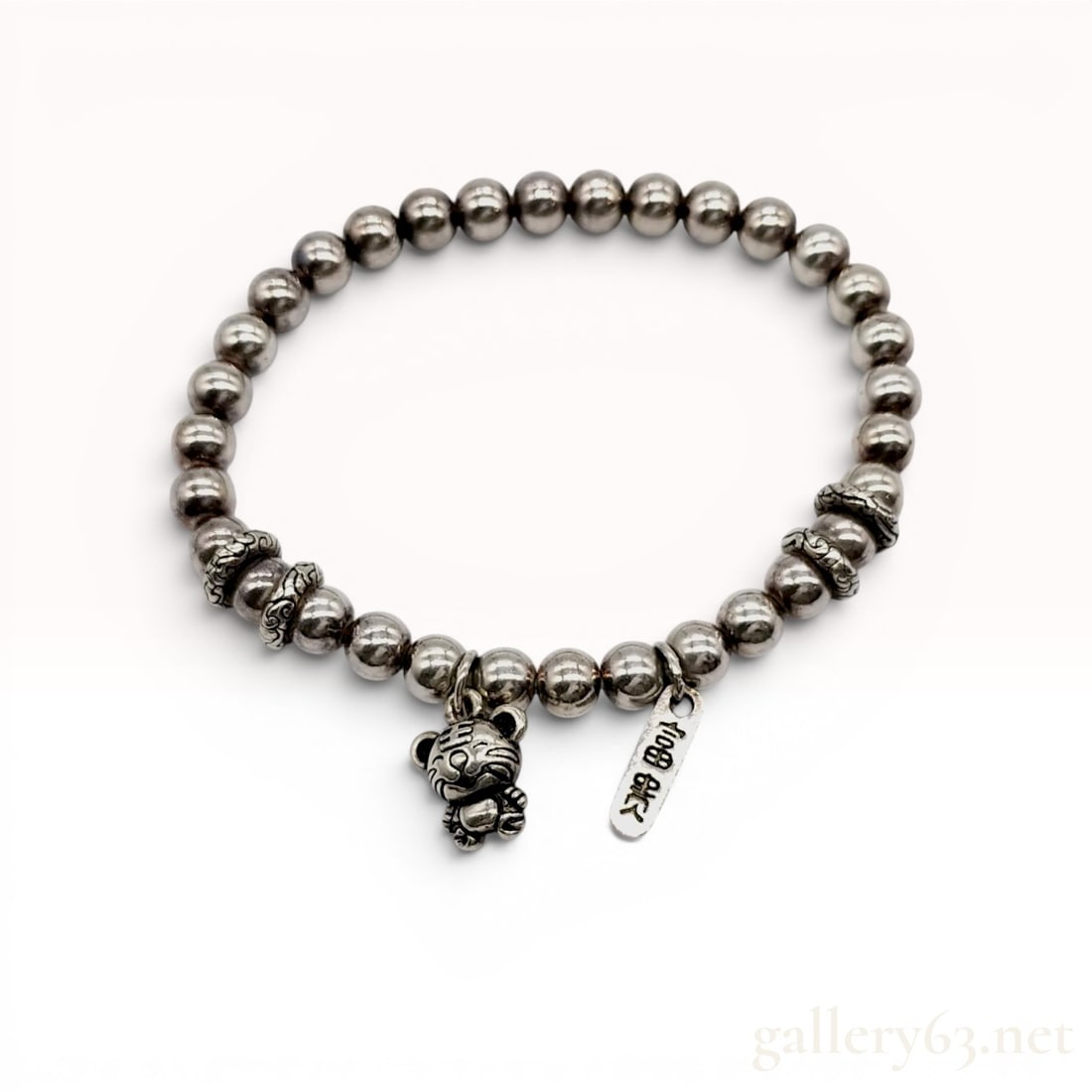Sterling Silver Beaded Charm Bracelet with Tiger and Inscribed Tag Charms: Sterling silver beaded charm bracelet featuring East Asian symbolic motifs. Constructed with polished silver round beads, four decorative antiqued scrollwork spacers, a stylized tiger charm marked wit
