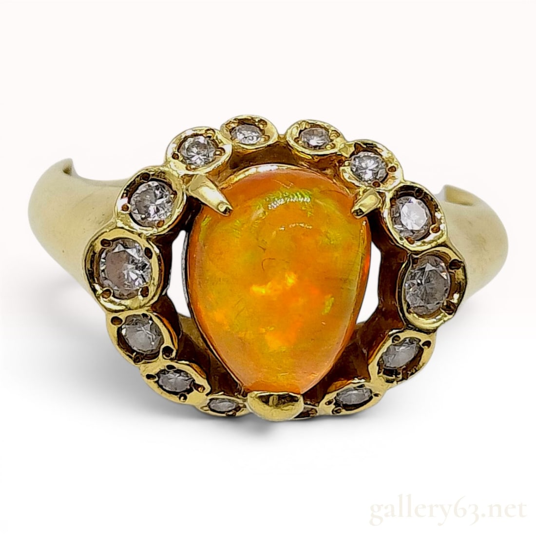 18K Yellow Gold Fire Opal and Diamond Cocktail Ring: An 18 karat yellow gold cocktail ring featuring a central pear-shaped cabochon-cut fire opal. The opal exhibits a vibrant orange body color with flashes of green and yellow play-of-color. The center s