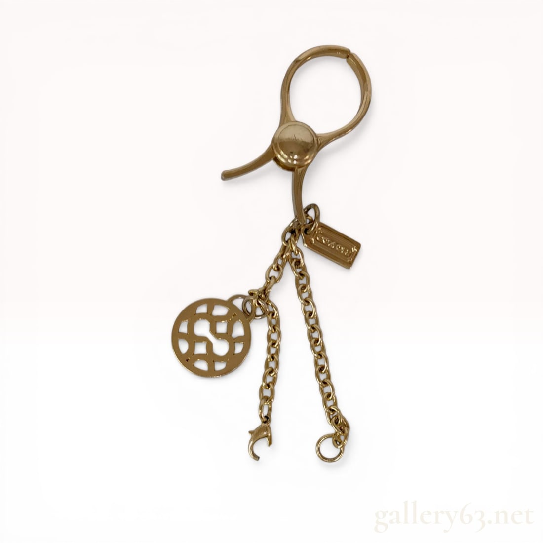 Coach Gold-Tone Glove Holder and Bag Charm: Coach gold-tone metal glove holder and bag charm set. The design features a large circular hinged spring clip, a signature C pattern cutout charm, and a rectangular Coach logo hangtag suspended from c