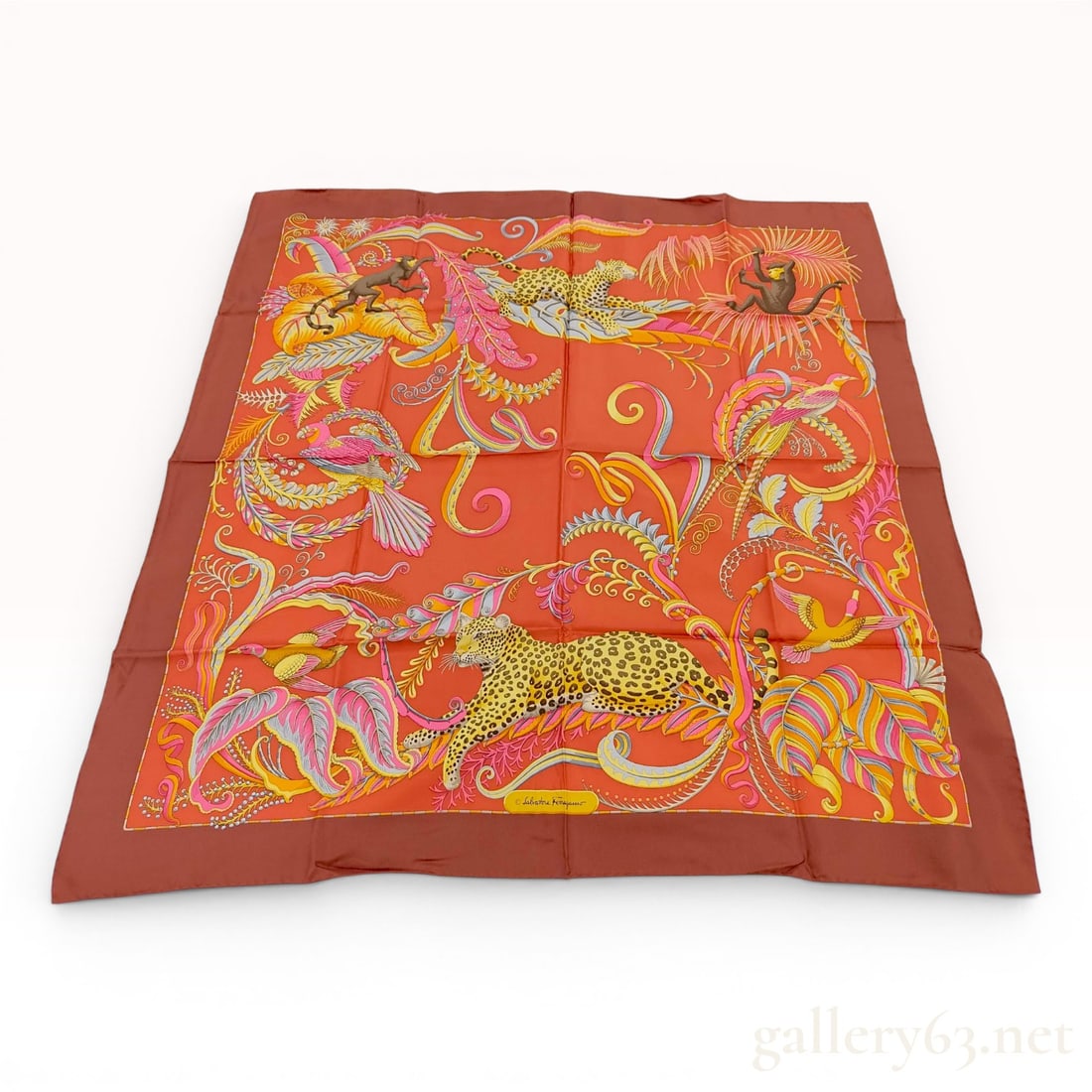 Salvatore Ferragamo Silk Twill Scarf with Jungle Wildlife Motif: A square silk twill scarf by Salvatore Ferragamo featuring a vibrant orange ground and dark burgundy border. The intricate design depicts a dense, stylized jungle scene with two leopards, two monkeys,