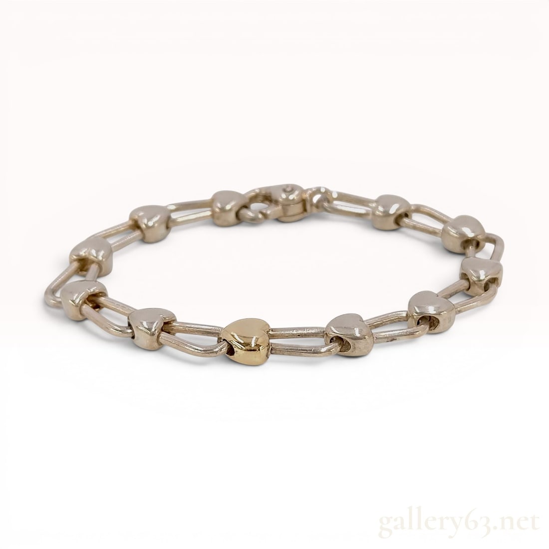Tiffany and Co. Sterling Silver and 18 Karat Yellow Gold Heart Link Bracelet: This link bracelet is a signature design from Tiffany and Co. featuring the puffed heart motif. The piece is constructed from.925 sterling silver with a single heart accent in 18 karat yellow gold. Th