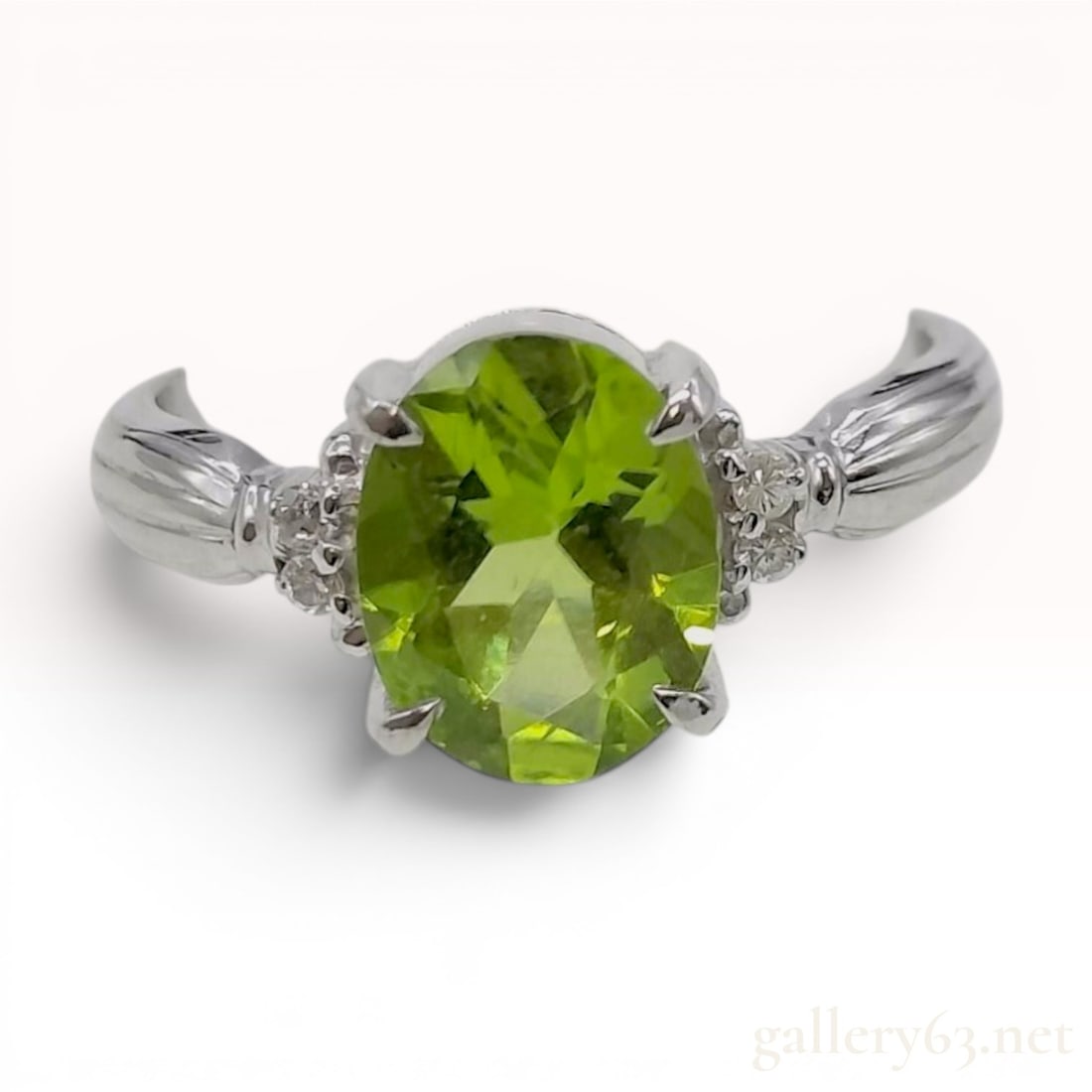 Peridot and Diamond Platinum Cocktail Ring: A platinum cocktail ring featuring a centrally mounted oval-cut peridot and accent diamonds. The peridot is held in a four-prong setting with double-claw tips. The shoulders are decorated with six sma