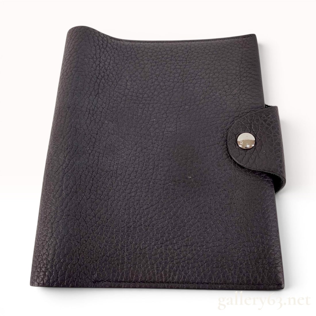 Hermes Ulysse PM Togo Leather Agenda Cover: This Hermes Ulysse PM agenda cover is crafted from dark brown Togo leather featuring a pronounced pebbled grain. The design includes a wrap-around tab with a polished silver-tone snap-button closure. 