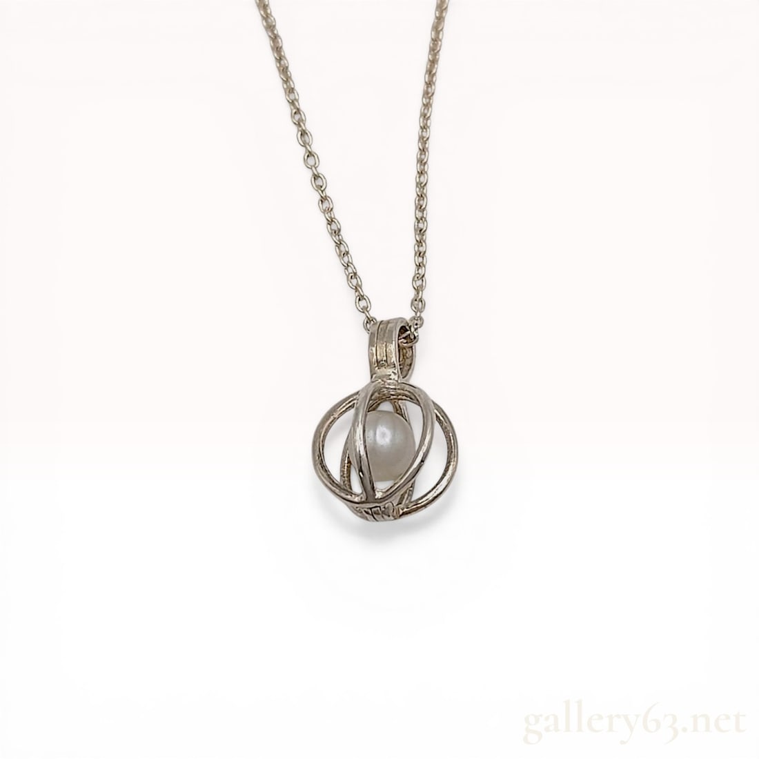 Sterling Silver and Cultured Pearl Cage Pendant Necklace: Sterling silver pendant necklace featuring a spherical hinged cage with three intersecting wires containing one cream-colored cultured pearl. The pendant is suspended from a fine cable link chain secu