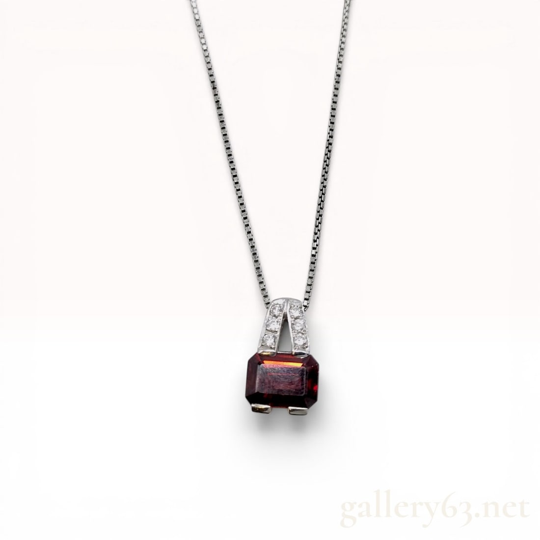 Platinum Emerald-Cut Garnet and Diamond Pendant Necklace: Platinum pendant necklace featuring a 1.50 carat emerald-cut garnet and 0.09 carats of accent diamonds. The rectangular red garnet is held in a four-prong basket setting below a bail pave-set with six