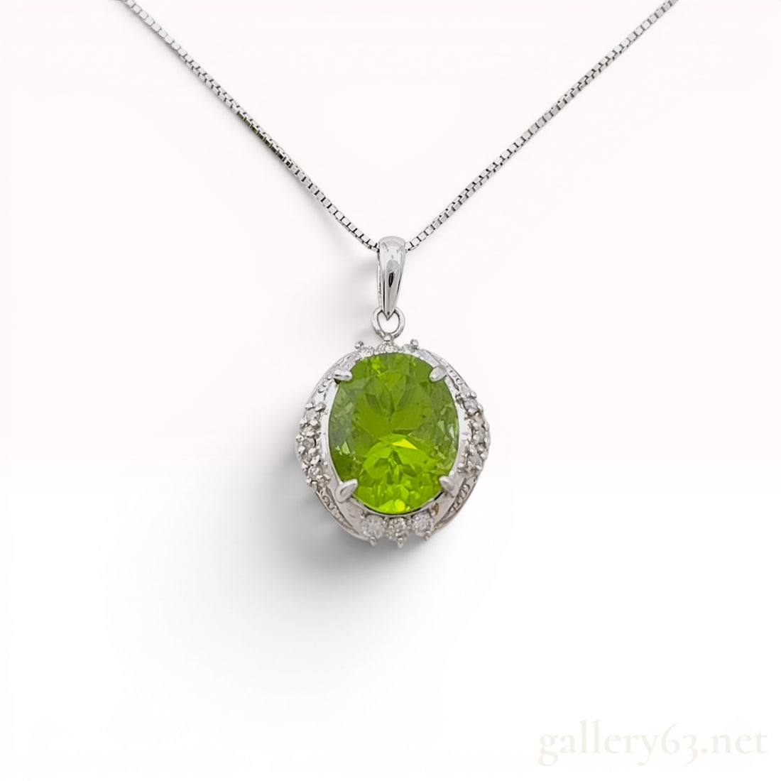 18K White Gold Peridot and Diamond Halo Pendant Necklace w/Box: An 18-karat white gold necklace featuring an oval-cut peridot and diamond halo pendant. The center gemstone is secured in a four-prong setting with a decorative openwork gallery, suspended from a box 
