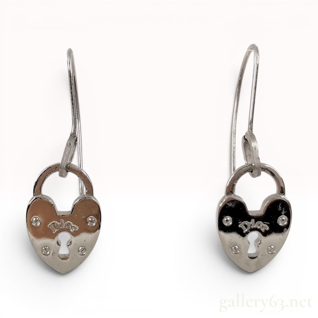 A Pair of Christian Dior Heart Padlock Drop Earrings: A matched pair of Christian Dior drop earrings featuring heart-shaped padlock charms. Each earring is crafted from polished silver-tone base metal and consists of a padlock pendant suspended from a Fr