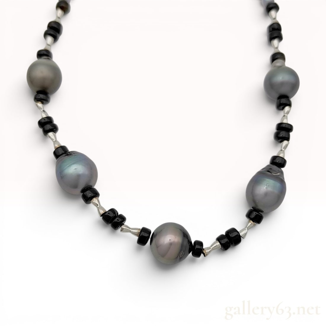 Graduated Black Cultured Pearl and Silver Necklace with Bow Clasp: A graduated bead necklace featuring cultured pearls and decorative metal elements. The front section is composed of five large baroque-shaped dark grey Tahitian-style cultured pearls exhibiting irides