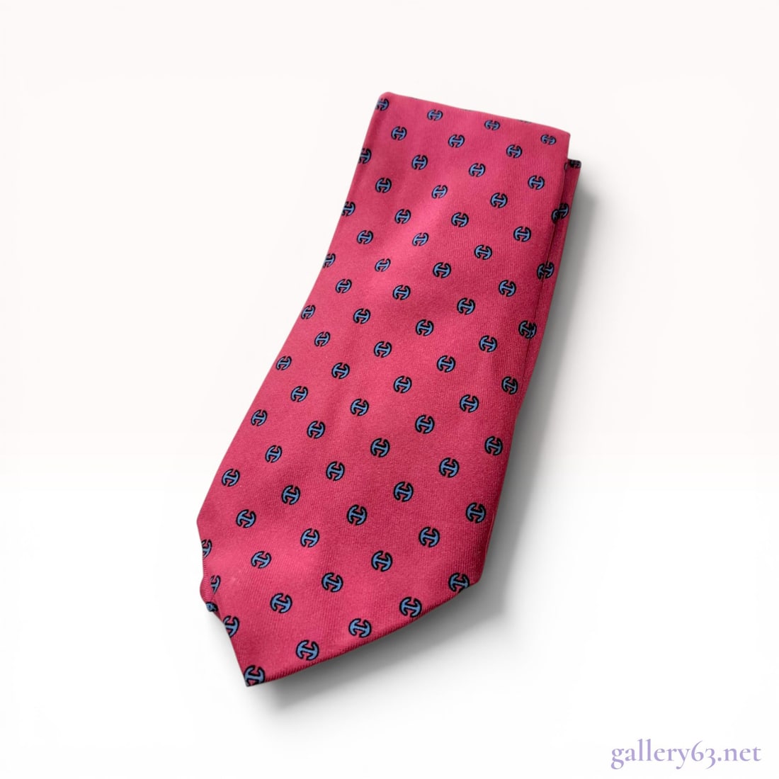 Hermes Silk Twill Geometric Pattern Necktie: Hermes silk twill necktie featuring a repeating geometric pattern of blue and black stylized H motifs on a reddish-pink ground. The reverse includes a printed label marked Made in France and 7029 TA, 